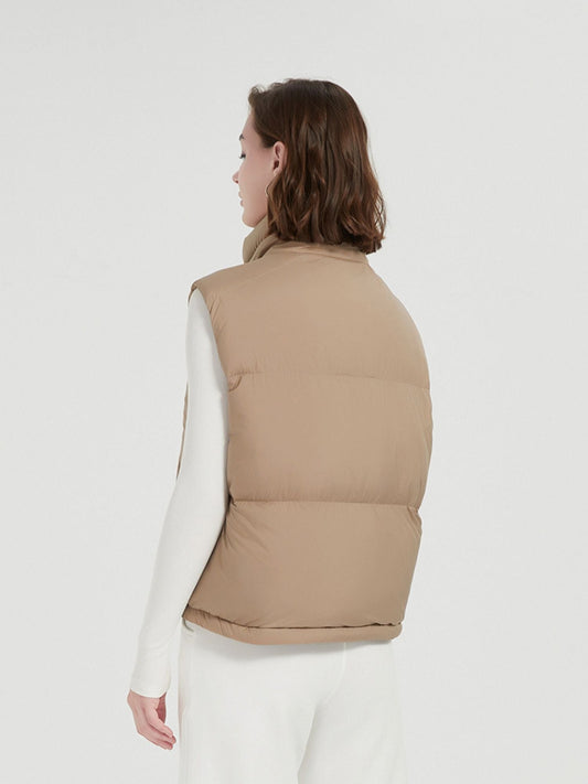 A female model wearing a quilted down vest with a stand collar in a beige color, paired with a white top and trousers with her back turned.
