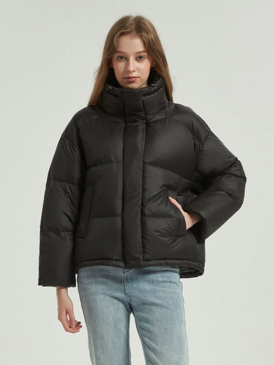 A female model wearing a black quilted down jacket with a stand collar, full zip, and functional pockets with the zipper closed completely.
