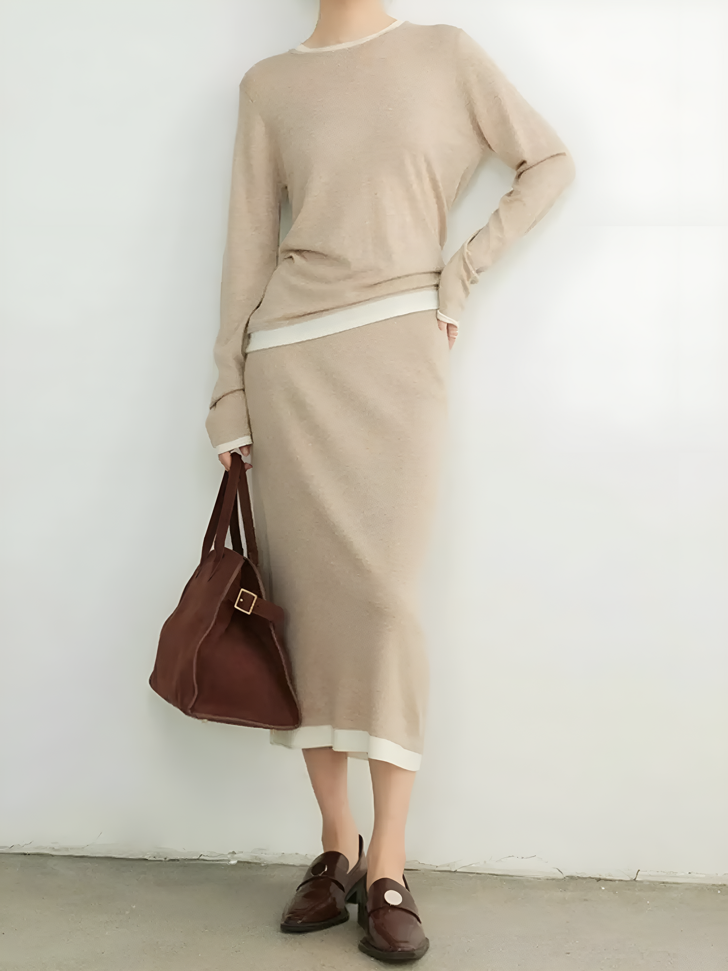 Person wearing a beige outfit with a brown bag against a white background