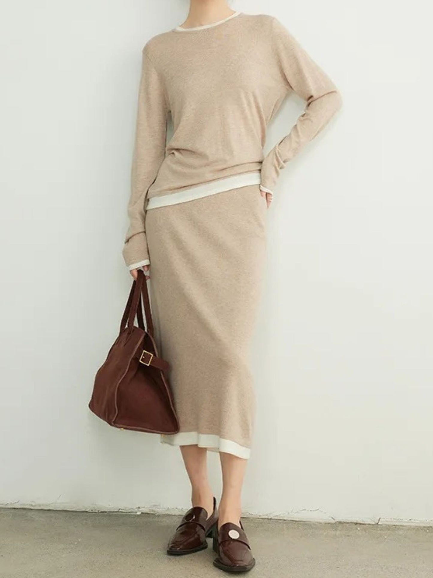 A woman wearing a khaki sweater and skirt with white details.