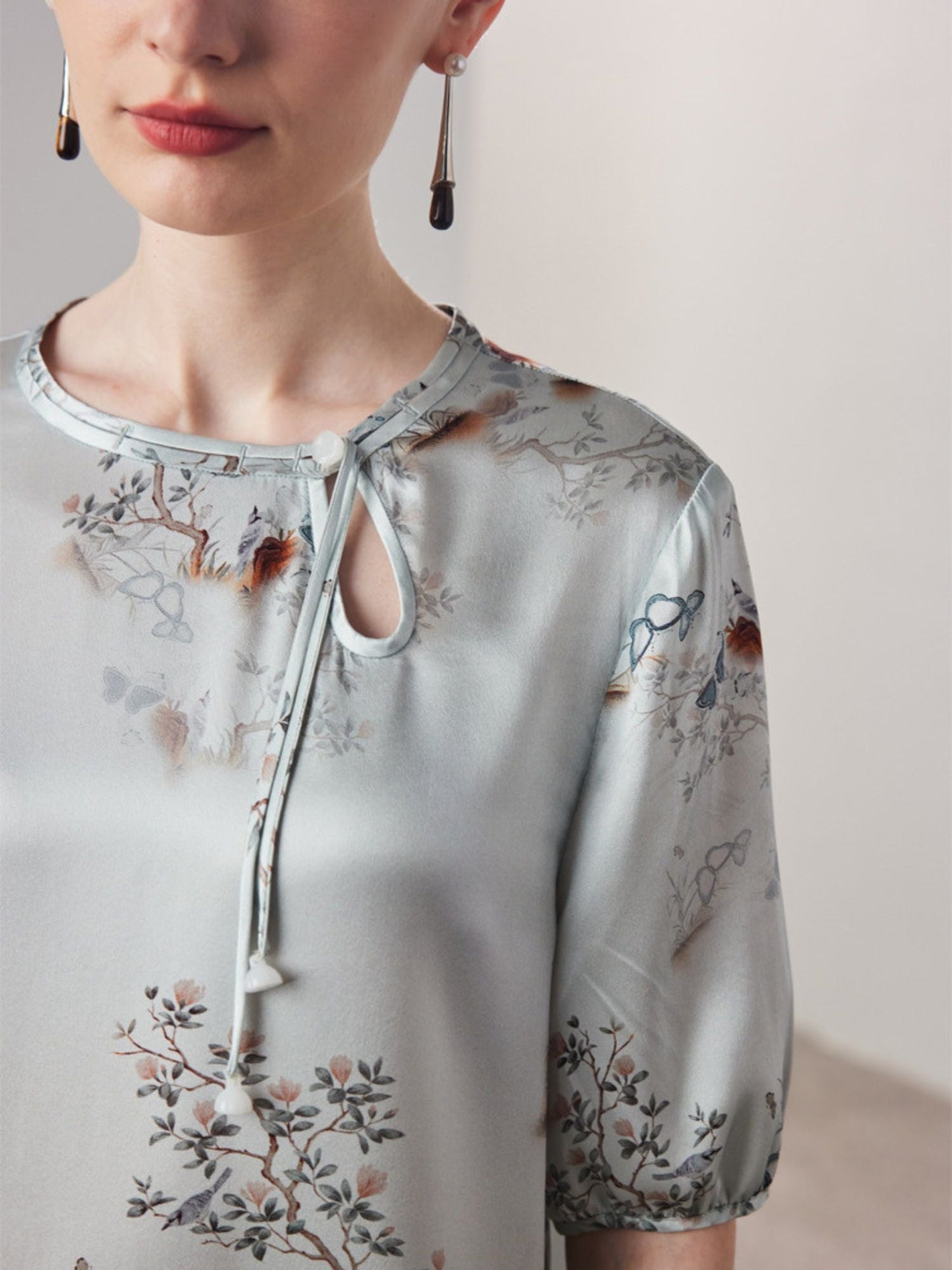 Close up of A woman wearing a grey silk-blend floral dress with a round neckline and 3/4-length sleeves.