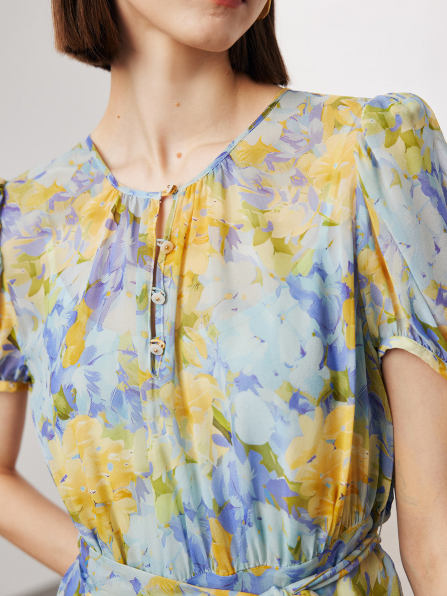 A close up of A floral silk dress with puffed sleeves and a tie waist, worn by a female model.