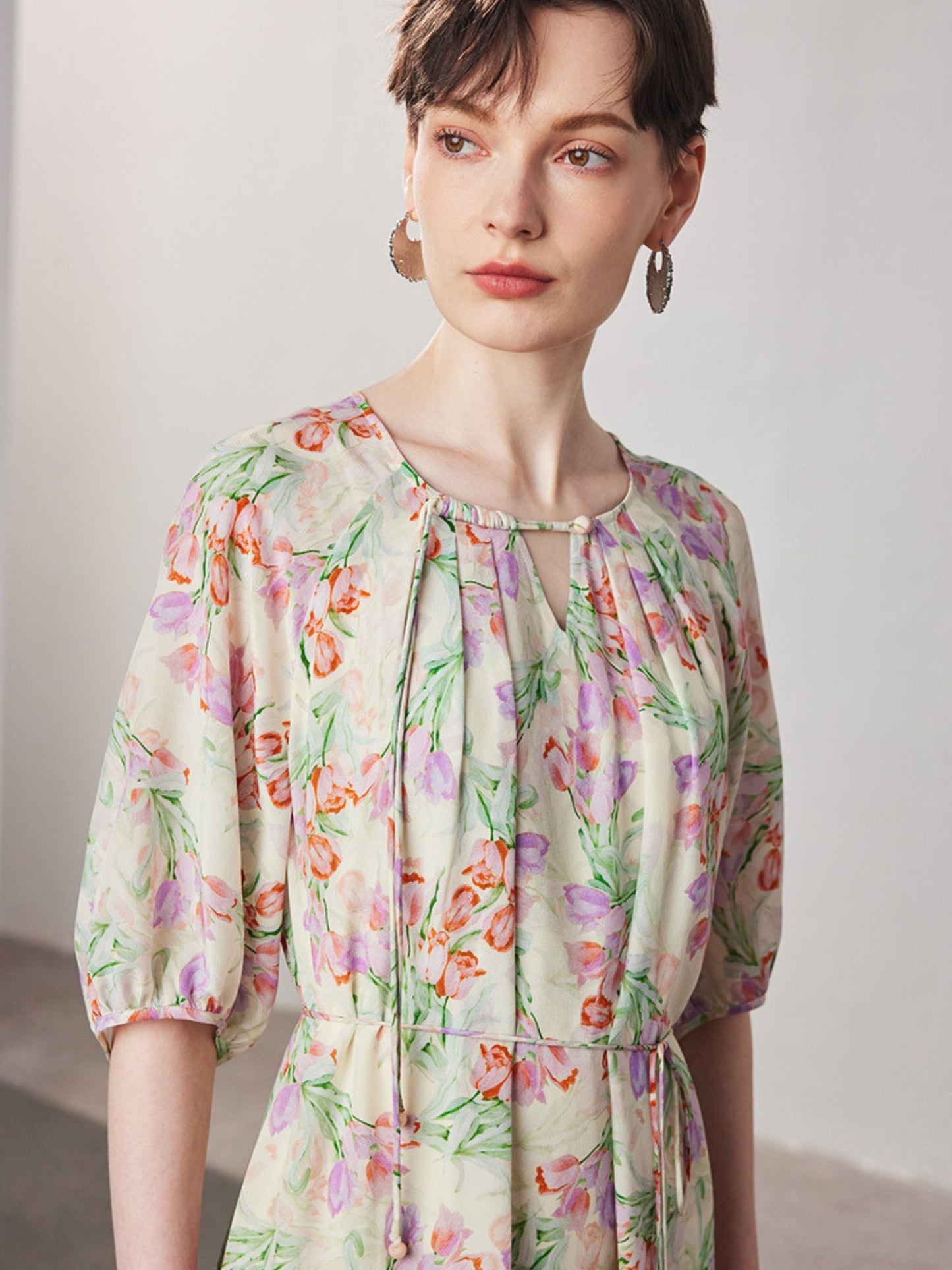 Close up of A woman modeling a floral silk dress with raglan sleeves and a straight silhouette, in a light color with a floral pattern.